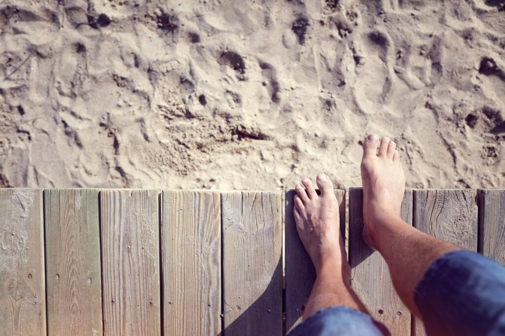 Man barefoot stepping off boardwalk onto the beach sand