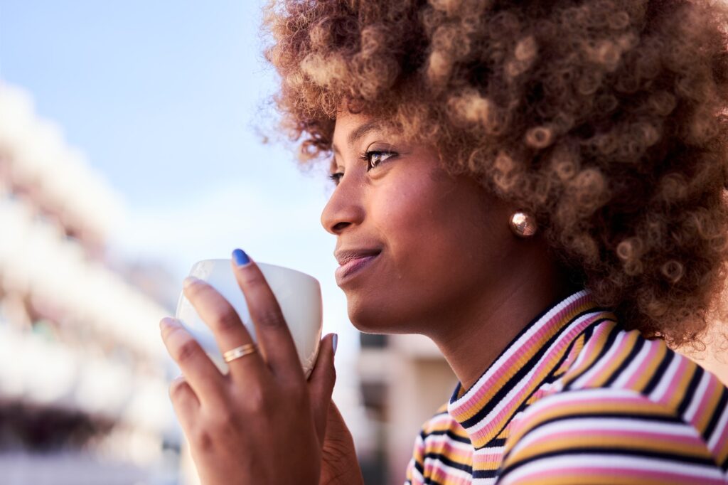 Young African woman drinking tea in her balcony in the morning enjoying the day and feeling relaxed.